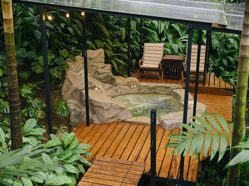Rock-edged jacuzzi and loungers on a covered forest deck